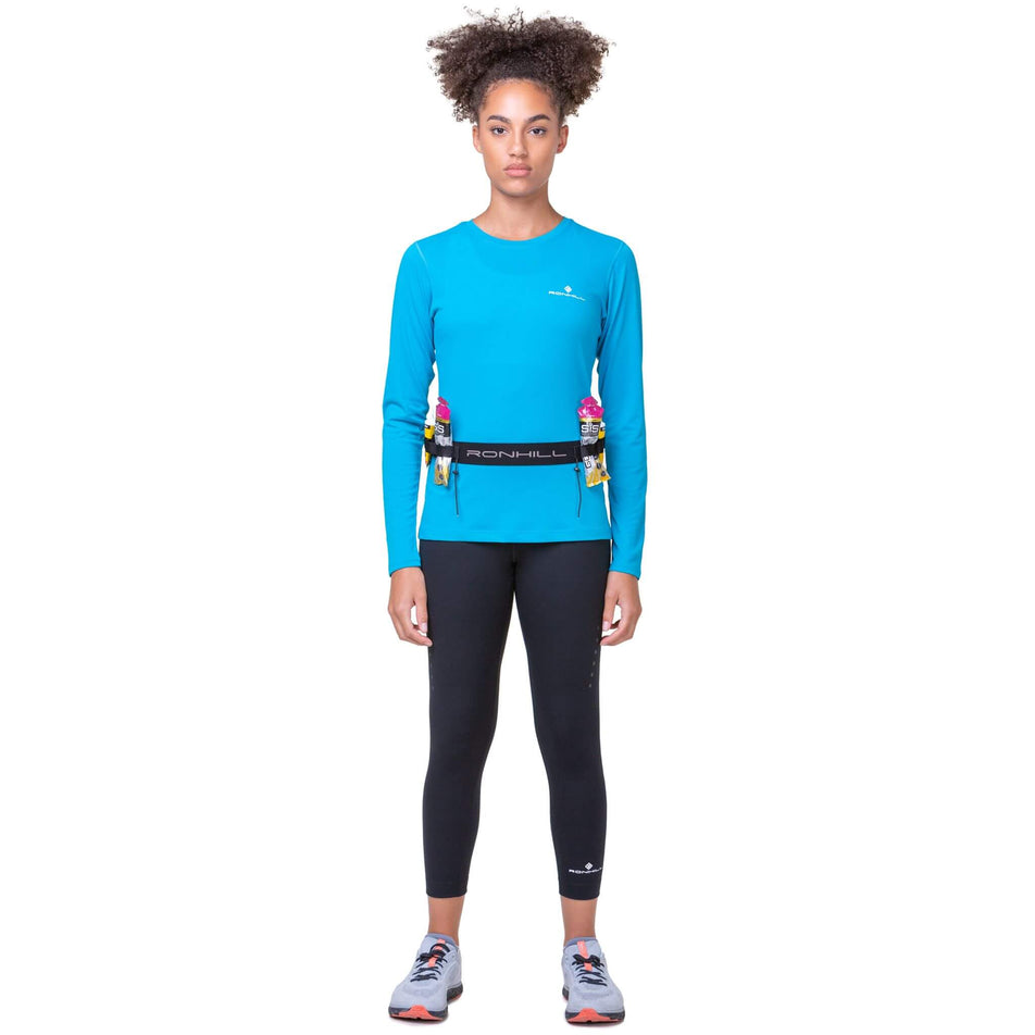 Front view of model wearing a Ronhill Race Number Belt. The model has energy gels in the belt's loops, and is wearing a top, leggings and shoes.  (8491326406818)