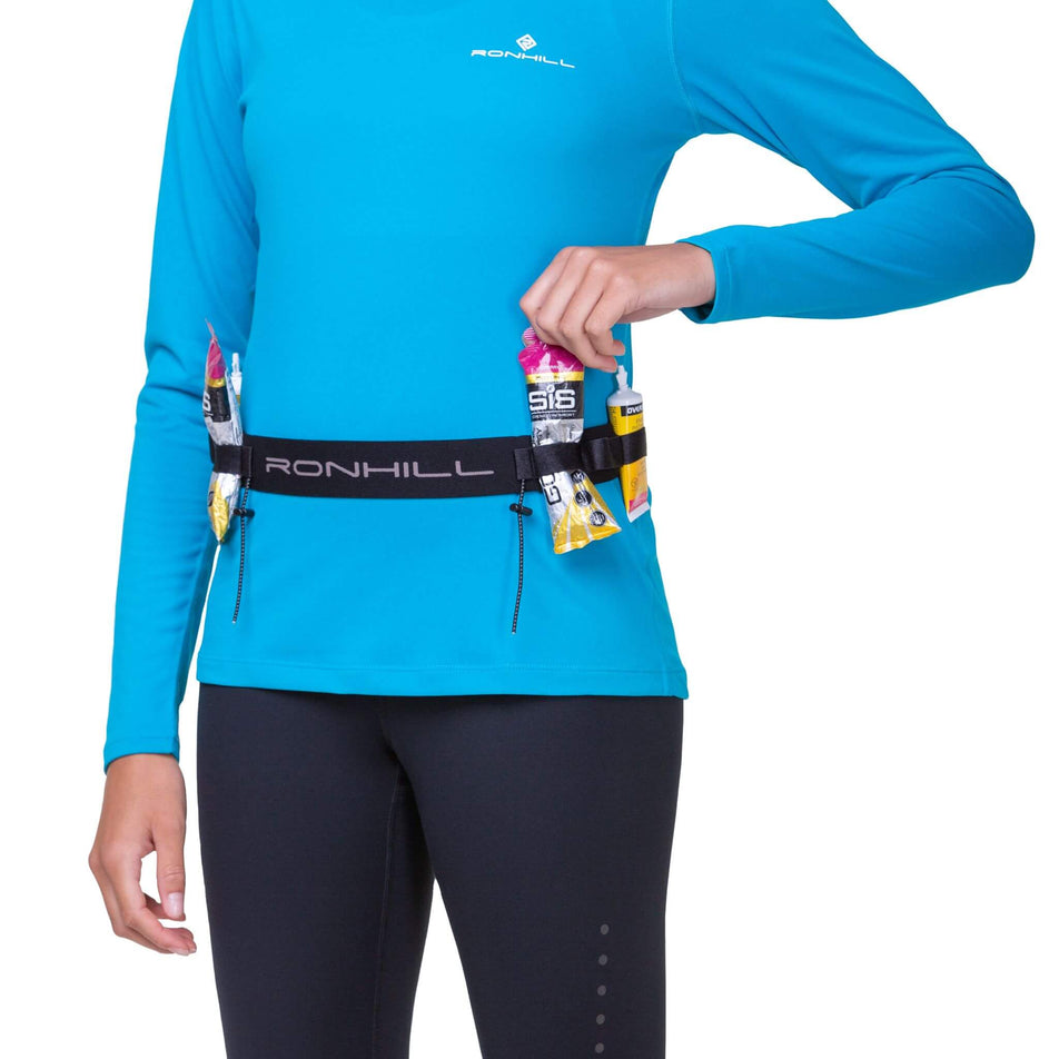 Front view of model wearing a Ronhill Race Number Belt. The model has energy gels in the belt's loops, and is wearing a top and leggings.  (8491326406818)