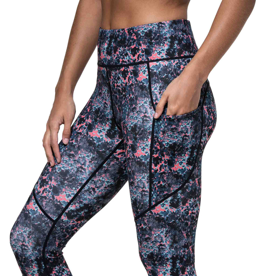 A model demonstrating the drop-in stash pocket on the side of the Ronhill Women's Tech Tight in the Coralescent colourway. (8747577770146)