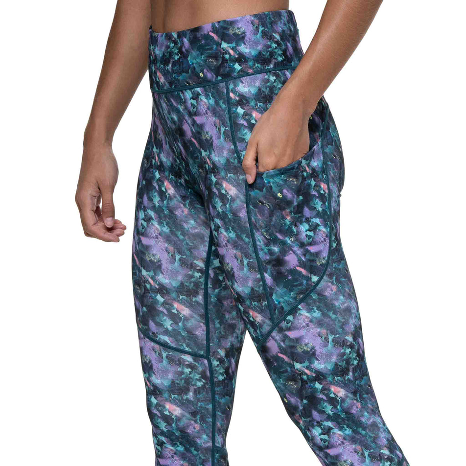 A model demonstrating the drop-in stash pocket on the side of the Ronhill Women's Tech Crop Tight in the Multi Flora colourway. (8747609784482)