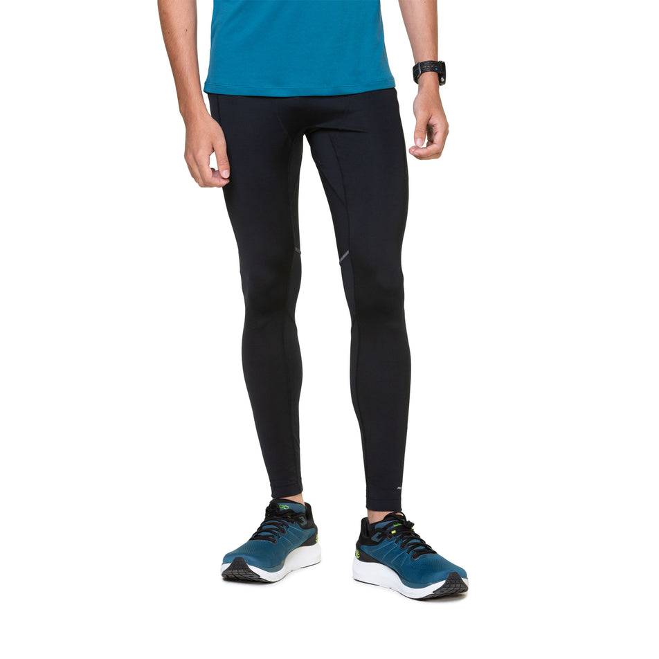 Front view of a model wearing the Ronhill Tech Paragon Tight in the All Black colourway. Model is also wearing shoes and a top. (8490275864738)