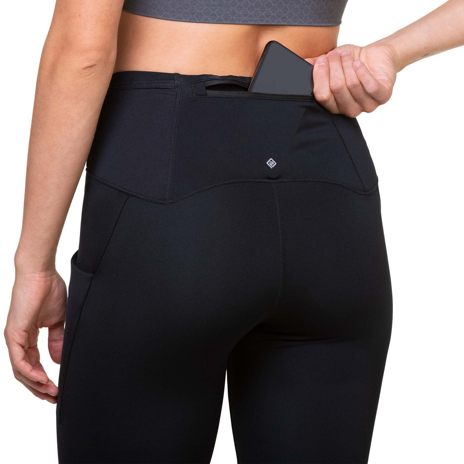 A model demonstrating that a phone can be stored in the back zip pocket of the Ronhill Women's Tech Paragon Tight. (8489936912546)