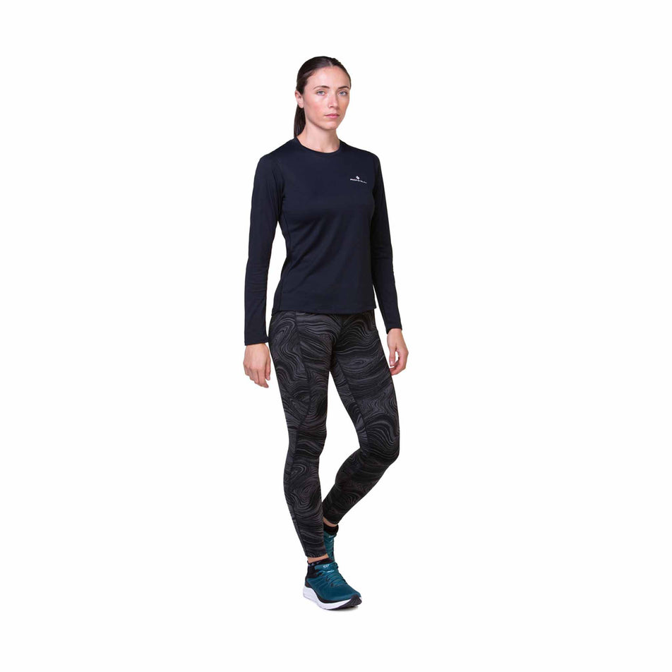 Front view of a model wearing the Ronhill Women's Tech Deluxe Tight in the Black/Charcoal colourway. Model is also wearing a long sleeve top, shoes and socks. (8469451112610)