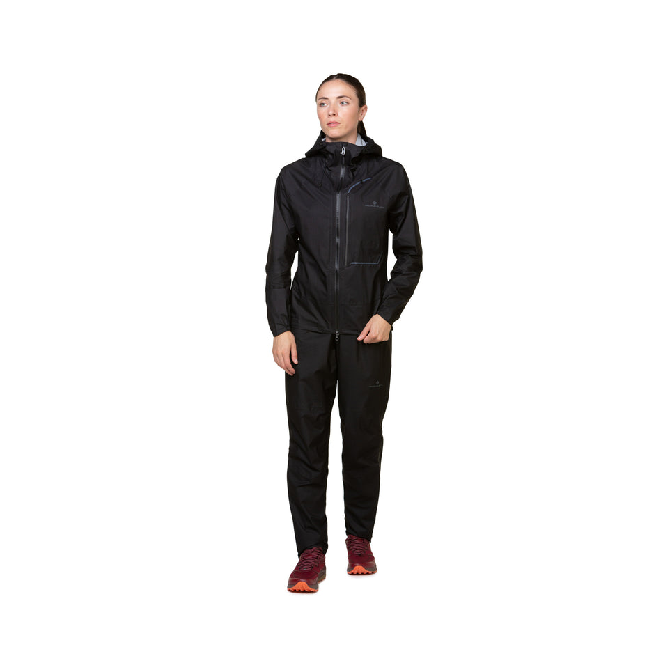 Front view of a model wearing a Ronhill Women's Tech Fortify Jacket in the All Black colourway. Model is also wearing shoes and trousers. (8489808429218)