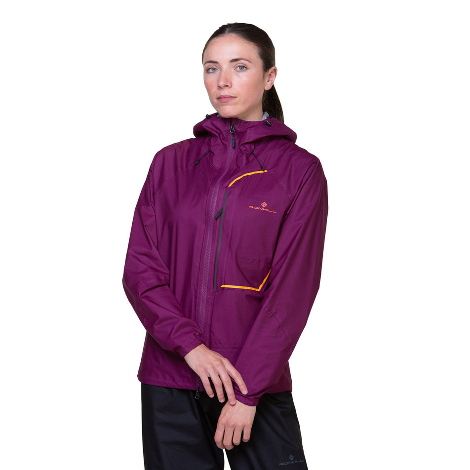 Front view of a model wearing a Ronhill Women's Tech Fortify Jacket in the Blackcurrant/Mango colourway. Model is also wearing trousers. (8469350121634)