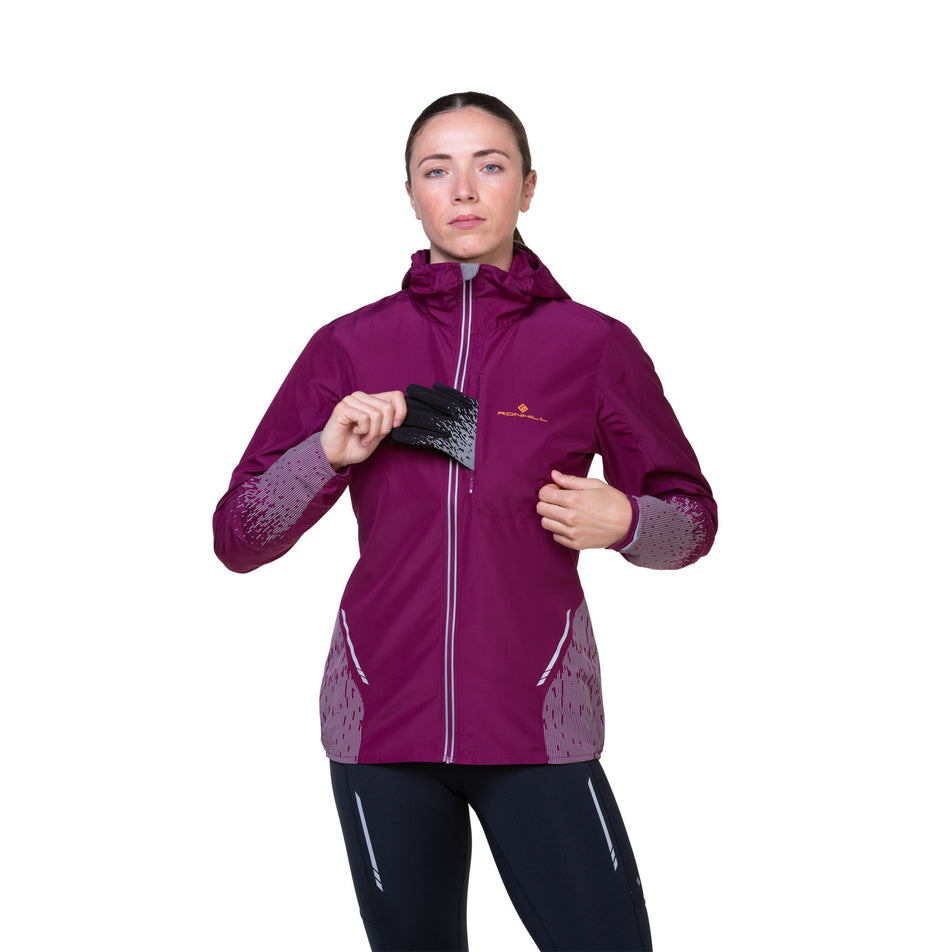Front view of a model highlighting that gloves can be stored in the chest pocket of a Ronhill Women's Tech Reflect Jacket in the Blackcurrant/Reflect colourway. Model is also wearing tights. (8489670607010)