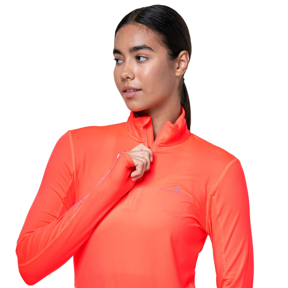 Front view of a model wearing the Ronhill Women's Tech Reflect 1/2 Zip in the Hot Coral/Reflect colourway. (8742195691682)