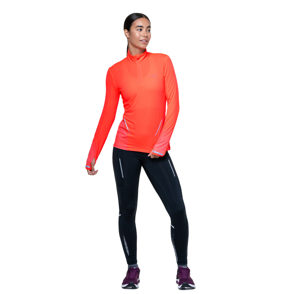 Front view of a model wearing the Ronhill Women's Tech Reflect 1/2 Zip in the Hot Coral/Reflect colourway. (8742195691682)