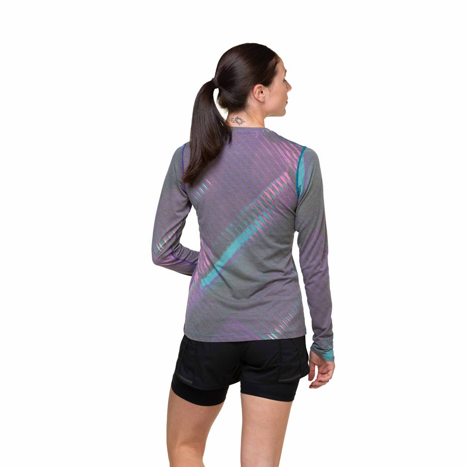 Back view of a model wearing the Ronhill Women's Tech Golden Hour L/S Tee in the Multi Light Reflection colourway. Model is also wearing shorts. (8490067361954)