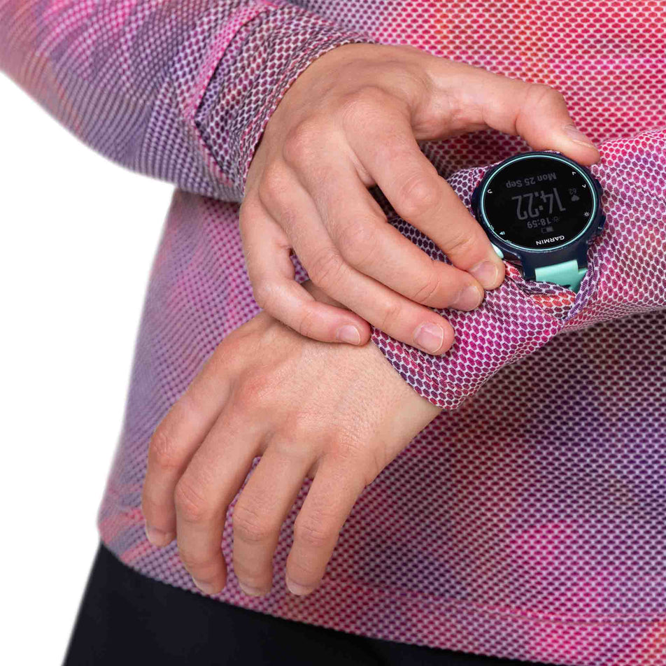 A model demonstrating that a running watch screen will fit through the gap in the fabric at the left-wrist of the Ronhill Women's Tech Golden Hour L/S Tee. (8490078666914)