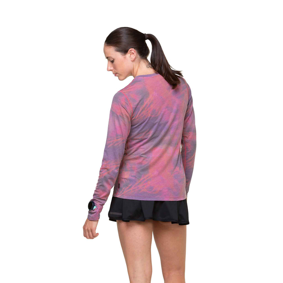 Back view of a model wearing the Ronhill Women's Tech Golden Hour L/S Tee in the Salsa Illuminations colourway. Model is also wearing shorts.  (8490078666914)