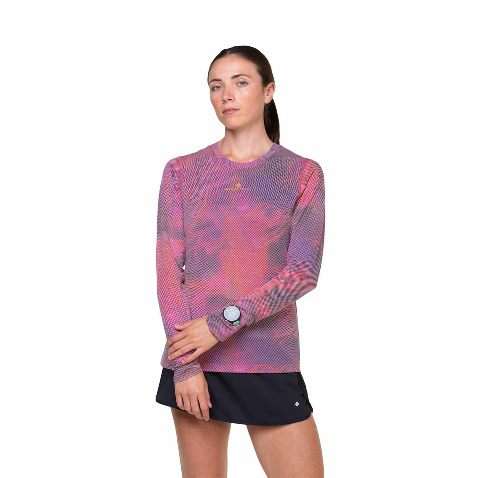 Front view of a model wearing the Ronhill Women's Tech Golden Hour L/S Tee in the Salsa Illuminations colourway. Model is also wearing shorts. (8490078666914)