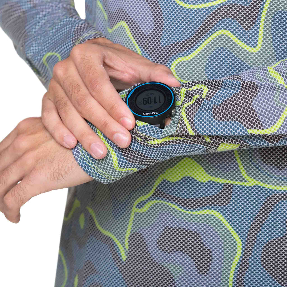 A model demonstrating that the screen of a running watch will fit through the gap in the left-sleeve on a Ronhill Men's Tech Golden Hour L/S Tee. Top is being worn by a model. (8490280550562)