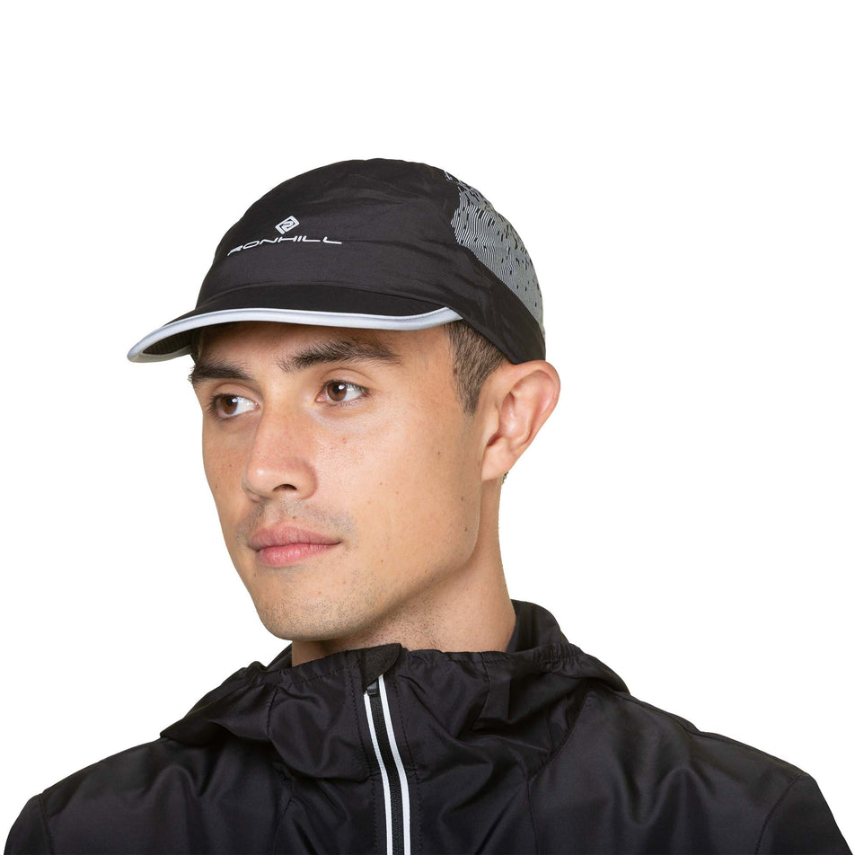 Front view of a model wearing the Ronhill Unisex Reflect Cap in the Black/Reflect colourway. Model is also wearing a jacket. (8491325358242)
