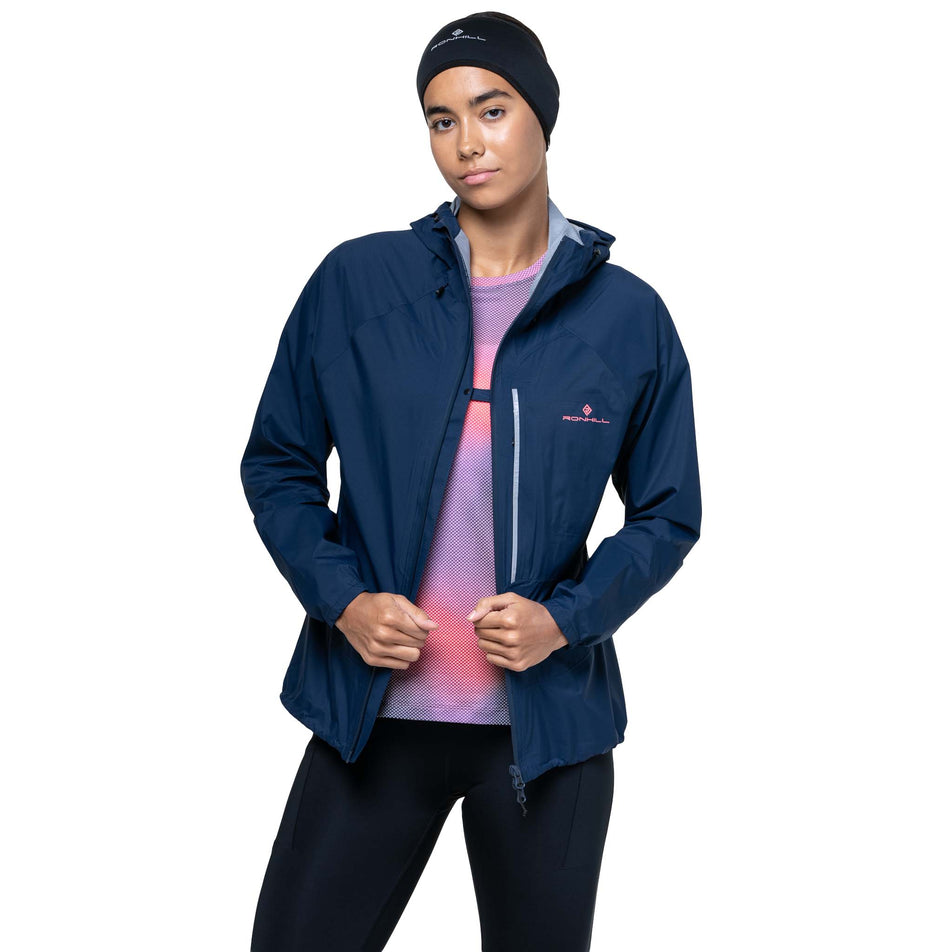 A model demonstrating the clip on the front of the Ronhill Women's Tech Storm Jacket in the Dark Navy colourway. (8742197559458)
