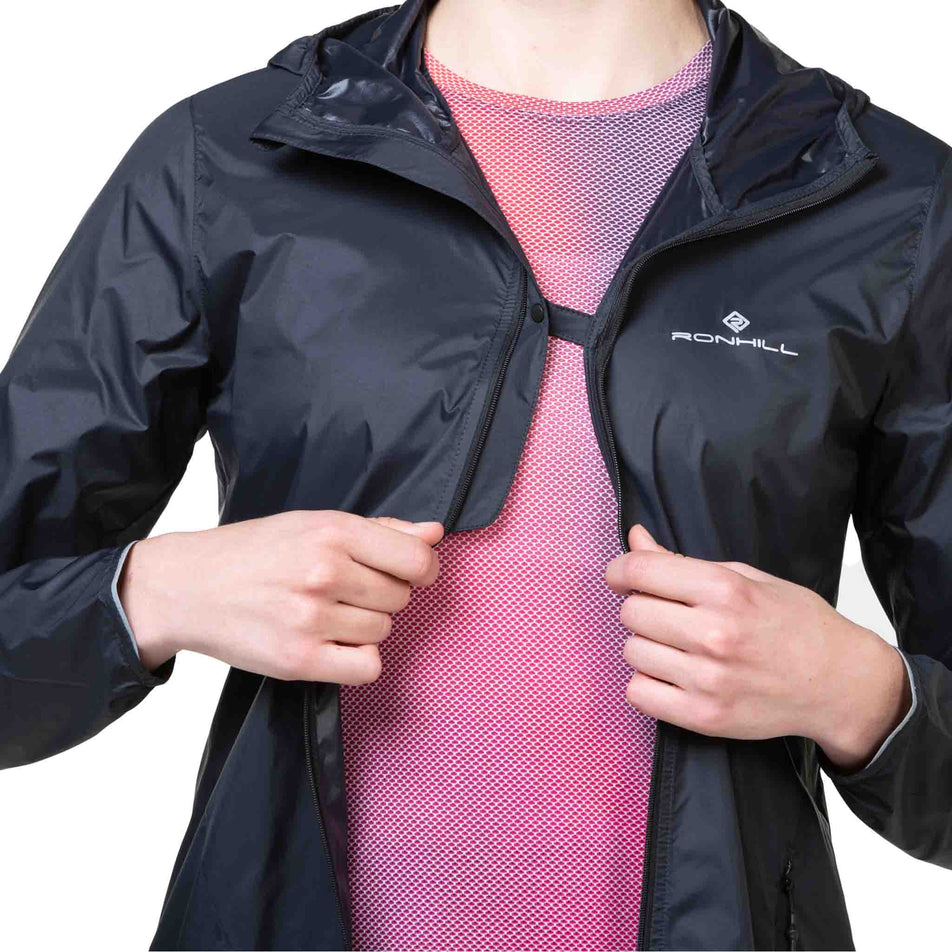 Front view of a model wearing the Ronhill Women's Tech All-Terrain Jacket in the All Black colourway with the chest clip attached. (8563593511074)