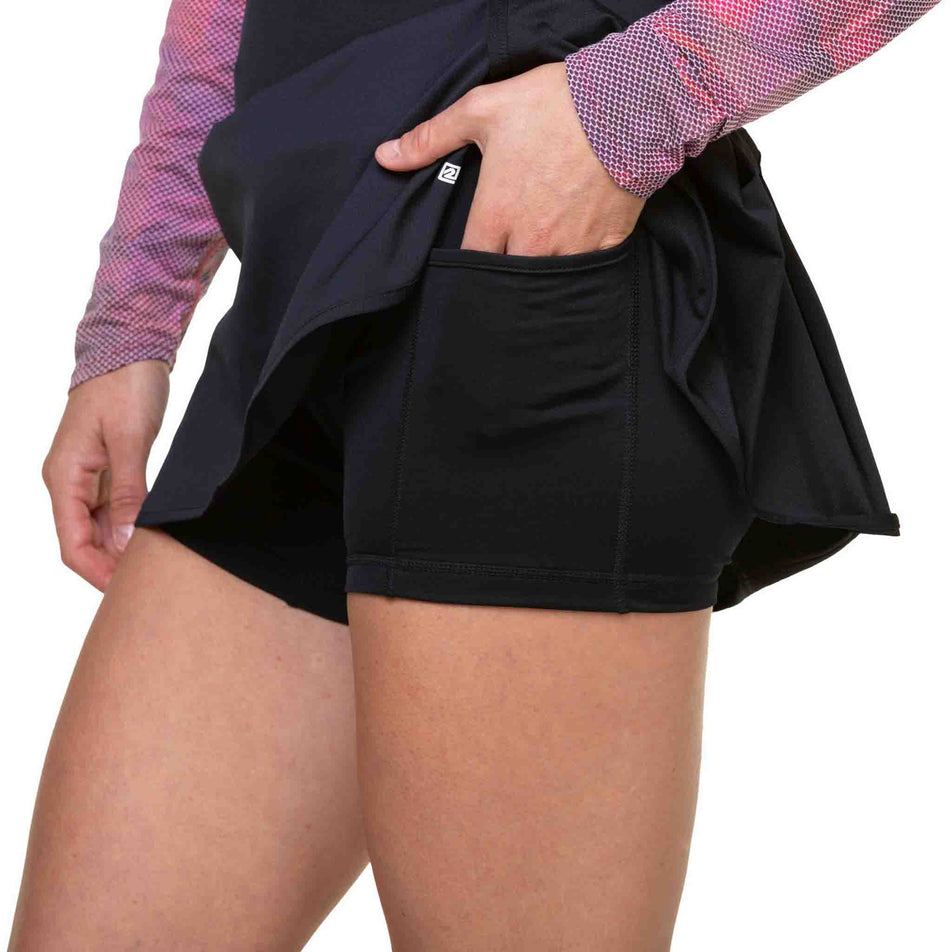 A model demonstrating the stash pocket on the liner of the Ronhill Women's Tech Skort in the All Black colourway. (8581024678050)