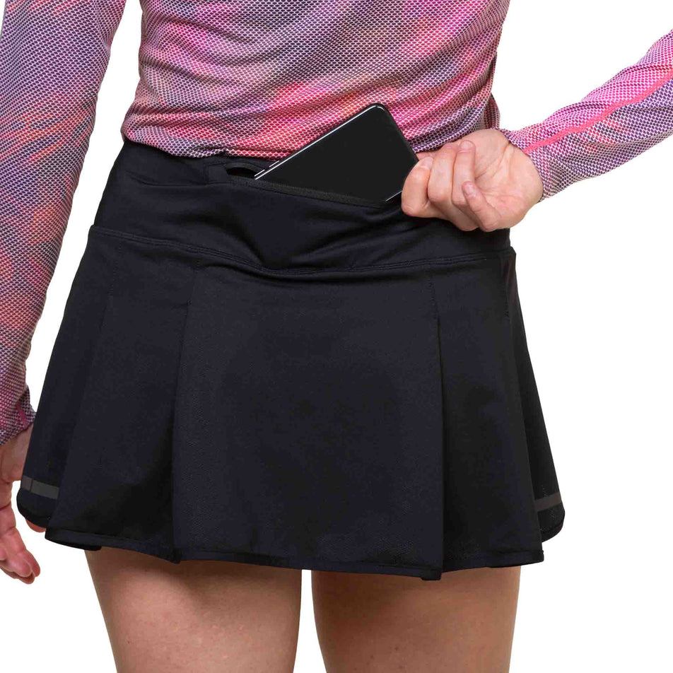 A model demonstrating the zip pocket on the back of the Ronhill Women's Tech Skort in the All Black colourway. (8581024678050)