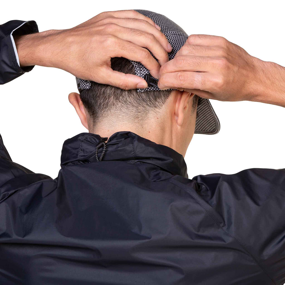 A model adjusting the toggle at the back of the Ronhill Unisex Golden Hour Cap in the Black Matrix colourway. (8587109793954)