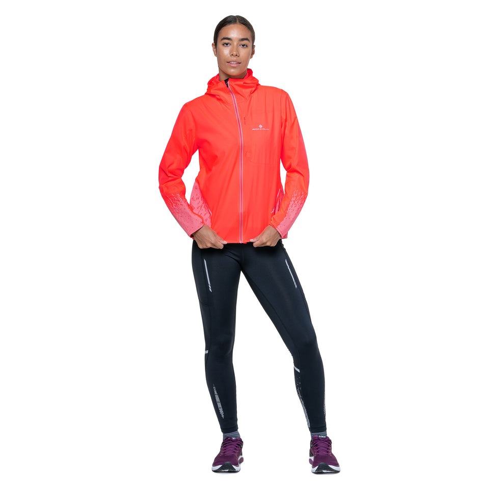 Front view of a model wearing the Ronhill Women's Tech Reflect Jacket in the Hot Coral/Reflect colourway.(8742191857826)