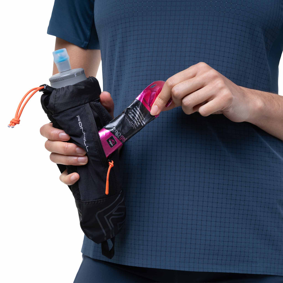 A model demonstrating the zip pocket on the Ronhill SoftFlask with Sleeve in the Black/Ronhill Red colourway.