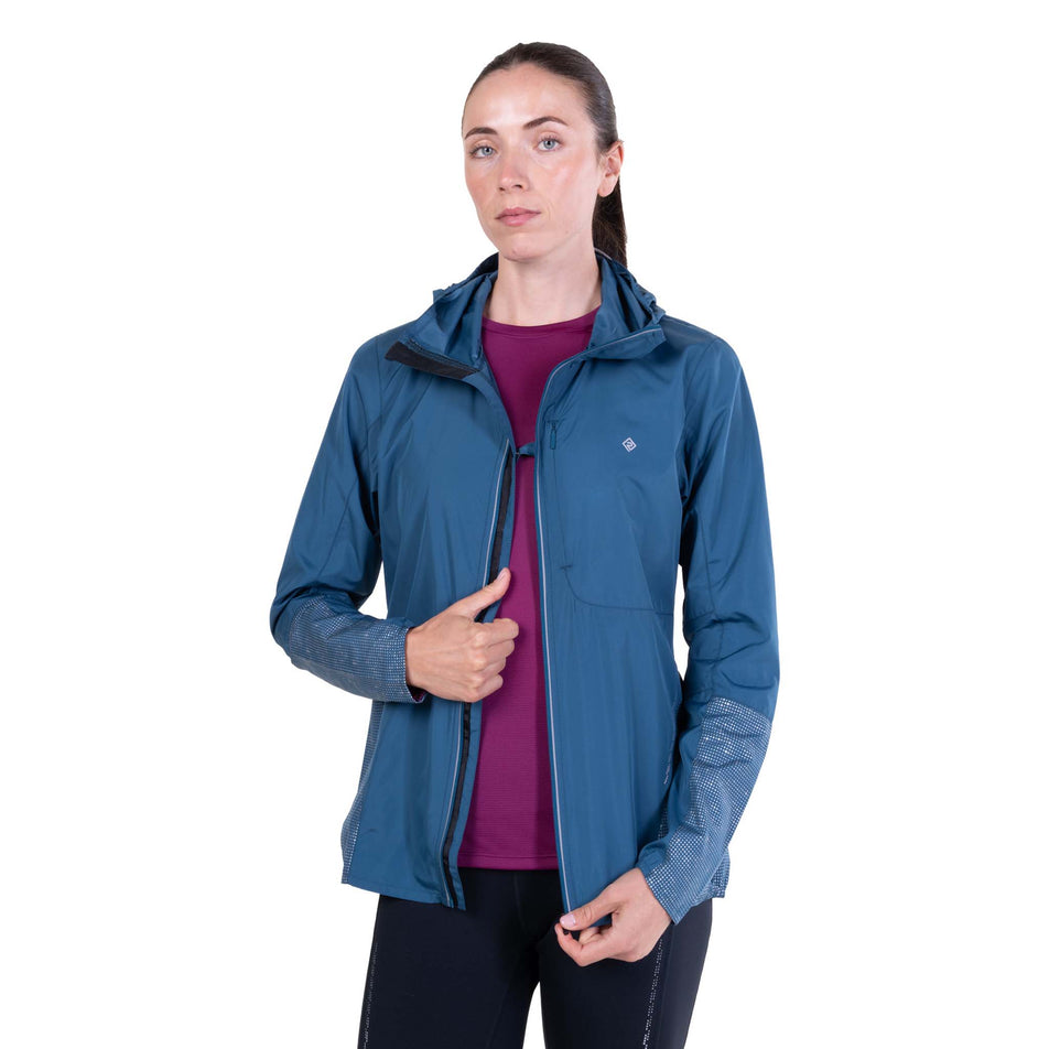 Front view of a model wearing the Ronhill Women's Tech Reflect Jacket in the Legion Blue/Reflect colourway with the chest clip attached.