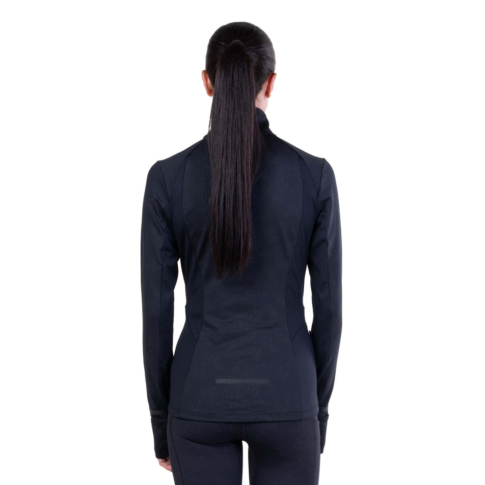 Back view of a model wearing the Ronhill Women's Tech Reflect Lux Jacket in the Black/Reflect colourway.