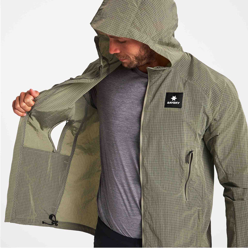 A model demonstrating the zippered vents on the SAYSKY Men's Clean Pace Shield Jacket in the Beige colourway.