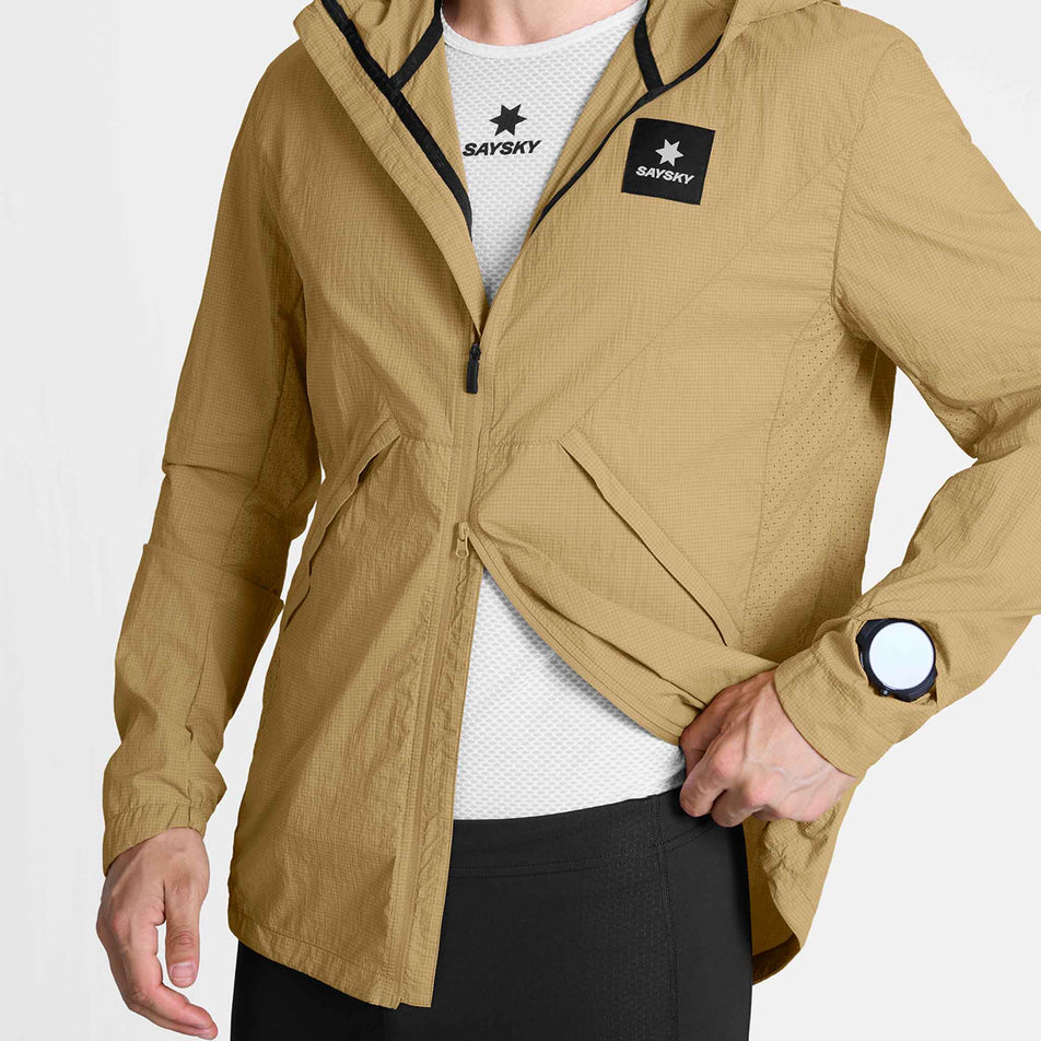 A model demonstrating the zipper function on the SAYSKY Men's Pace Tech Jacket in the Beige colourway.