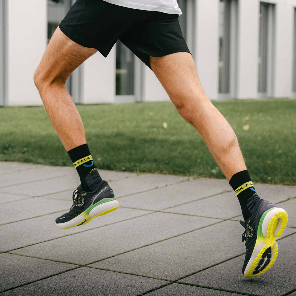 A model running in a pair of True Motion Men's U-TECH Nevos 3 in the Black/Asphalt/Evening Primrose colourway. (8618621304994)