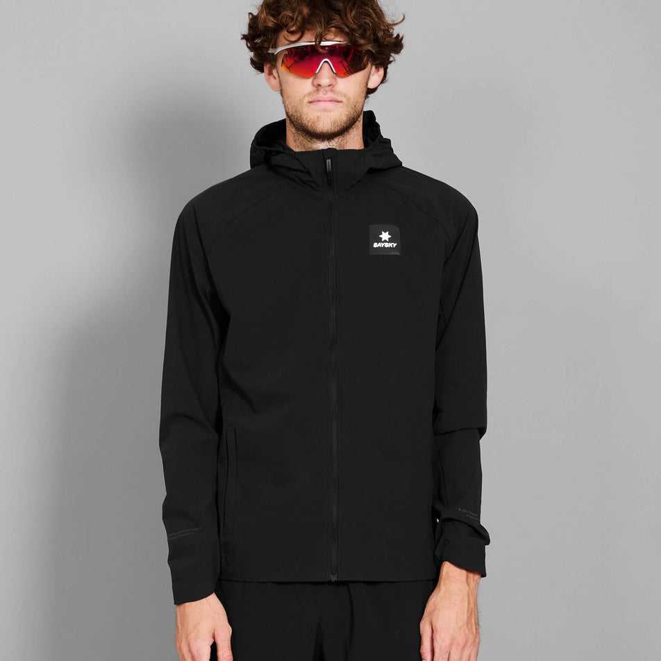 Front view of a model wearing the SAYSKY Men's Clean Pace Flex Hooded Jacket in the Black colourway. Model is also wearing sunglasses and trousers. (8601312362658)
