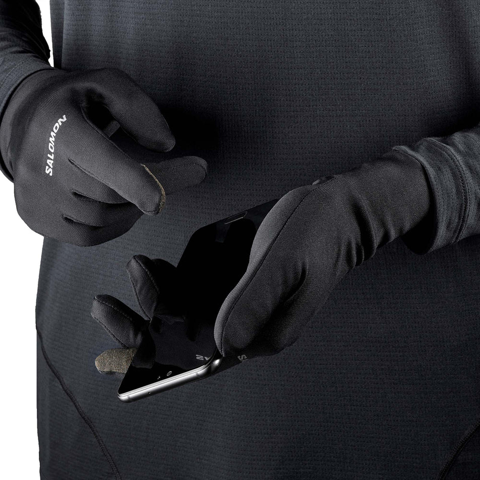 A model showing that a pair of Salomon Unisex Cross Warm Gloves are designed to allow you to use your smartphone with your gloves on. (7776505888930)