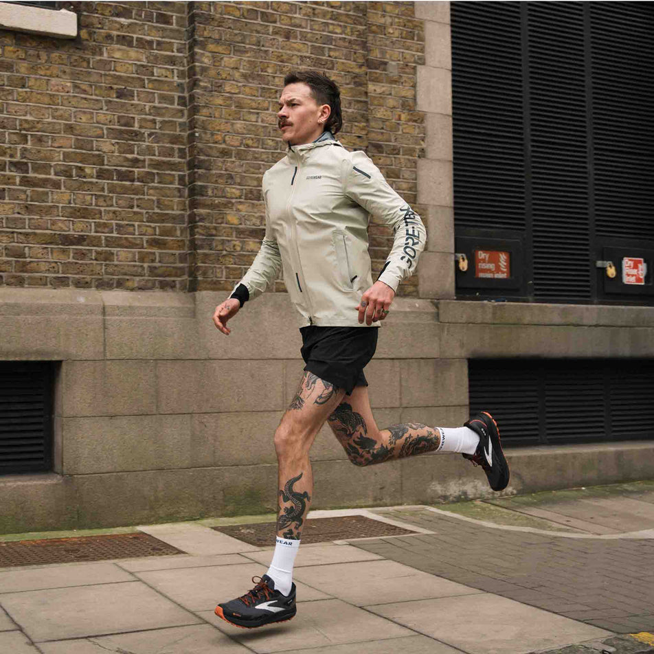 A model running in the GOREWEAR Men's Concurve GORE-TEX Logo Jacket in the Tech Beige/Black colourway. (8751737962658)