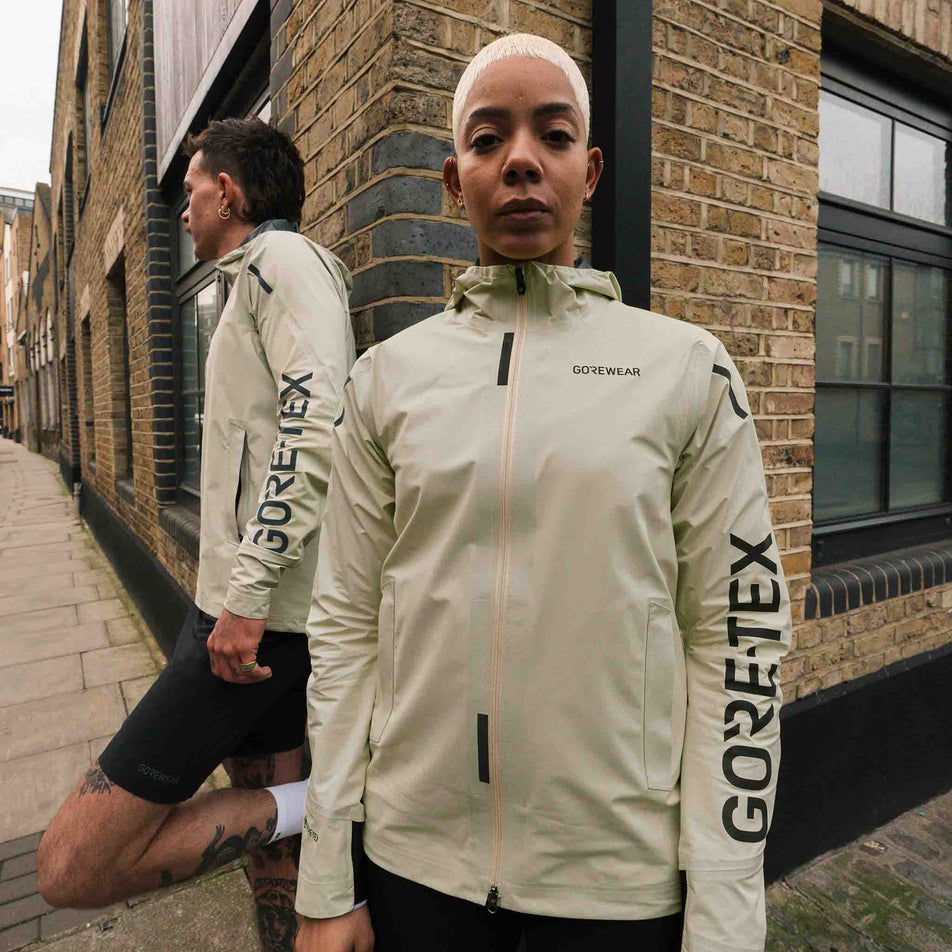 Front view of a model wearing the GOREWEAR Women's Concurve GORE-TEX Logo Jacket in the Tech Beige/Black colourway. (8752081207458)