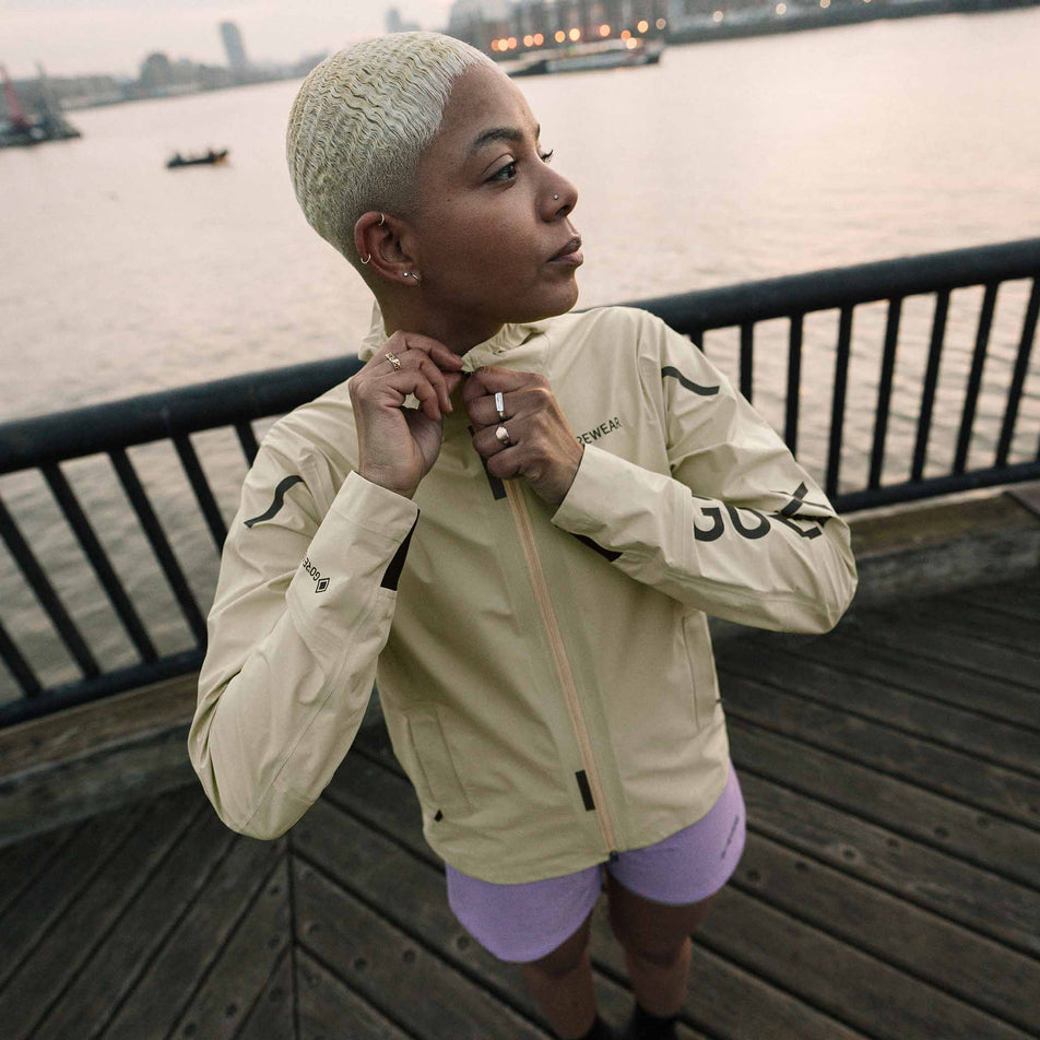 Front view of a model wearing the GOREWEAR Women's Concurve GORE-TEX Logo Jacket in the Tech Beige/Black colourway. (8752081207458)