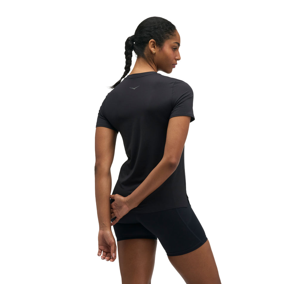 Back view of a model wearing the HOKA Women's Everyrun Short Sleeve in the Black colourway.