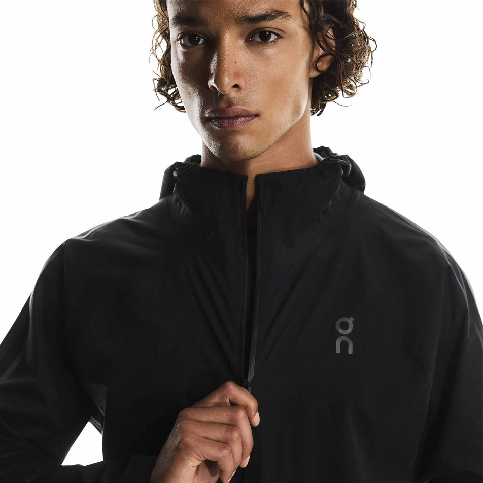 A model adjusting the zip on the On Men's Performance Waterproof Jacket in the Black colourway. (8790101819554)