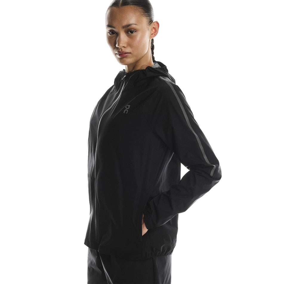 Angled view of a model wearing the On Women's Performance Waterproof Jacket in the Black colourway. (8790002696354)