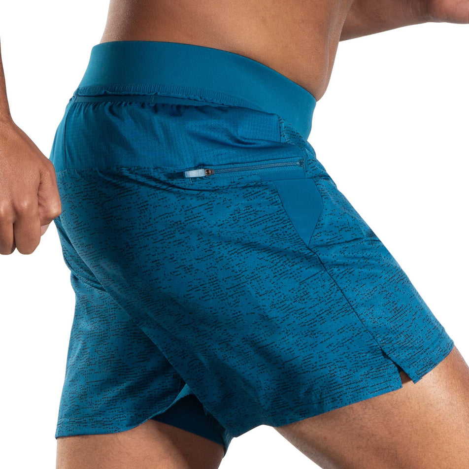 Side view of a model wearing a pair of Brooks Men's Sherpa 7 Inch 2-in-1 Shorts in the Dark Ocean Terrain Print colourway. Model is in a running pose.  (8007477133474)