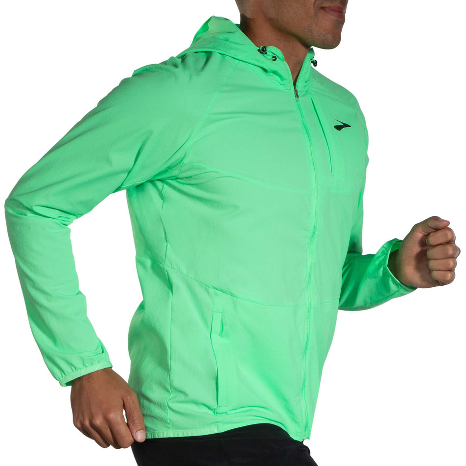 Angled front view of a model wearing a Brooks Canopy Running Jacket in the Neo Green colourway. Model is in a running pose. (8007418314914)