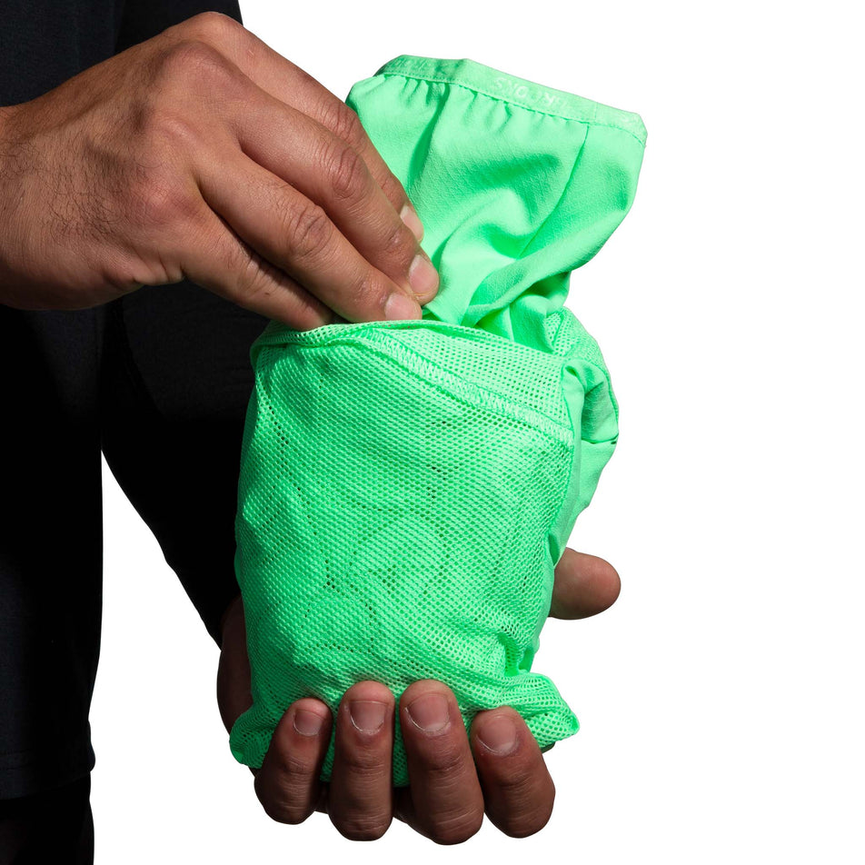 A model demonstrating that a Brooks Men's Canopy Jacket, in the Neo Green colourway, can be stuffed into one of its pockets.  (8007418314914)