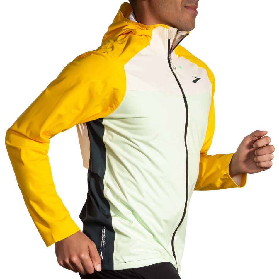 Side view of a model wearing a Men's High Point Waterproof Jacket in the Glacier Green/Ecru/Lemon colourway. Model is also wearing Brooks legwear. (8177405821090)