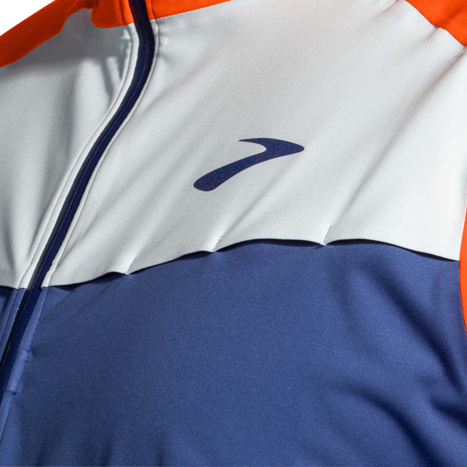 The left-side of the chest section of a Brooks Men's High Point Waterproof Jacket in the Aegean/Bright Orange/Lt Slate colourway. Jacket is being worn by a model. (8037731270818)
