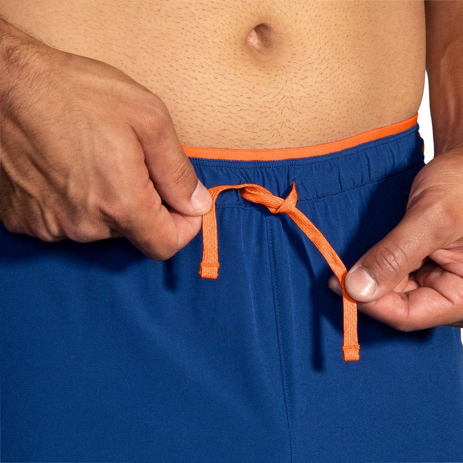 A model demonstrating that there is a drawcord on the outside of the front of a pair of Brooks Men's High Point 7