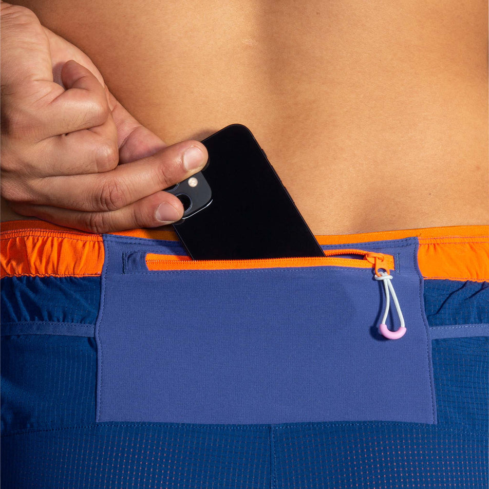 A model demonstrating that there is a zipped back pocket - capable of storing a phone - on a pair of Brooks Men's High Point 7