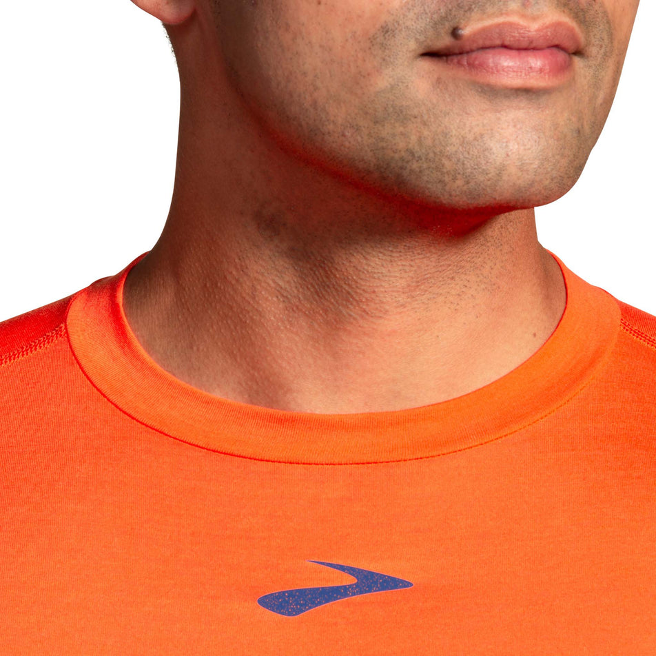 Close-up view of the neck detail and Brooks logo on a Brooks Men's High Point Long Sleeve Top in the Bright Orange colourway. Top is being worn by a model. (8037726814370)