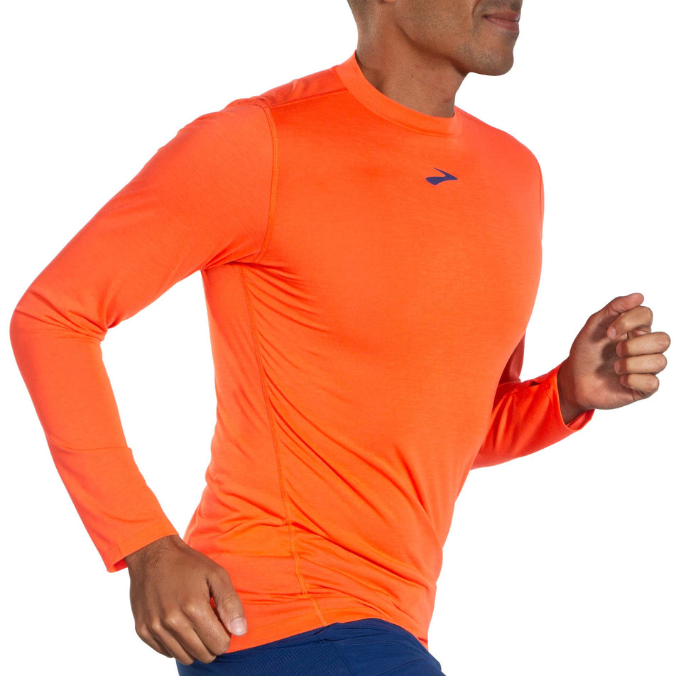 Right-side view of a model wearing a Brooks Men's High Point Long Sleeve Top in the Bright Orange colourway. Model is in a running pose. (8037726814370)