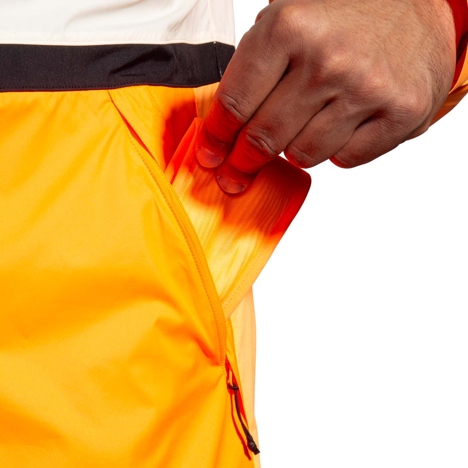 Left zippered pocket on the front of the Brooks Men's Run Visible Jacket 2.0 in the Ecru/Fluoro Flash/Black colourway. (8499396804770)