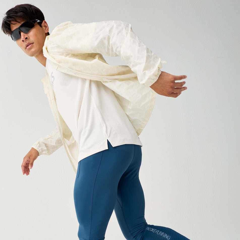 Angled view of a model wearing the Brooks Men's Canopy Reflective Jacket in the Reflective Wordmark Bone colourway.