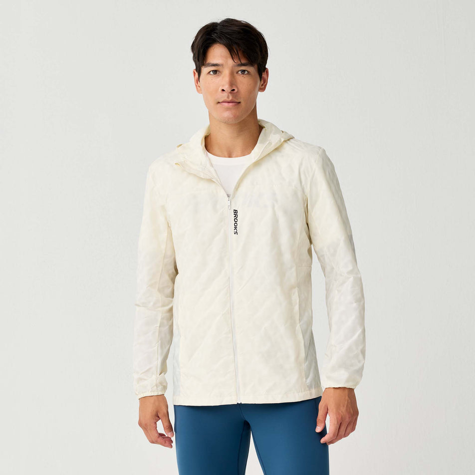 Front view of a model wearing the Brooks Men's Canopy Reflective Jacket in the Reflective Wordmark Bone colourway.